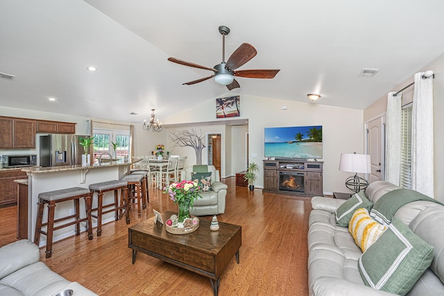 living room with ceiling fan with notable chandelier, light hardwood / wood-style floors, lofted ceiling, and a fireplace