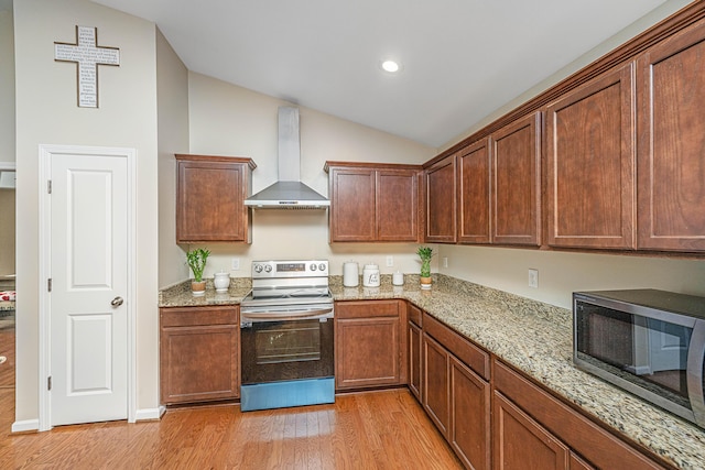 kitchen with appliances with stainless steel finishes, light stone counters, vaulted ceiling, wall chimney range hood, and light hardwood / wood-style floors