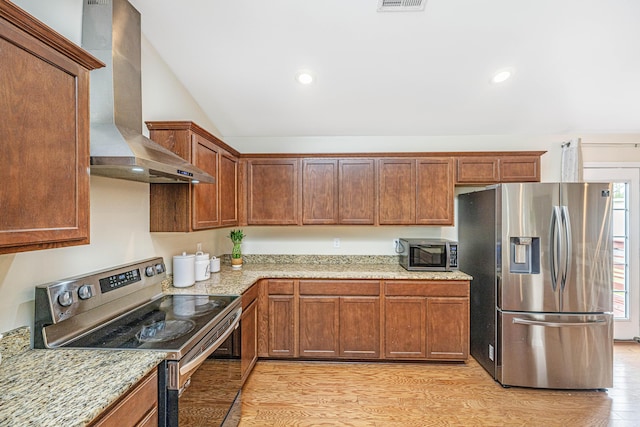 kitchen with wall chimney exhaust hood, light stone counters, light wood-type flooring, and appliances with stainless steel finishes