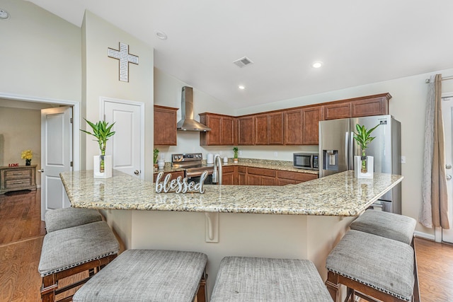 kitchen featuring lofted ceiling, dark wood-type flooring, a kitchen breakfast bar, wall chimney exhaust hood, and stainless steel appliances