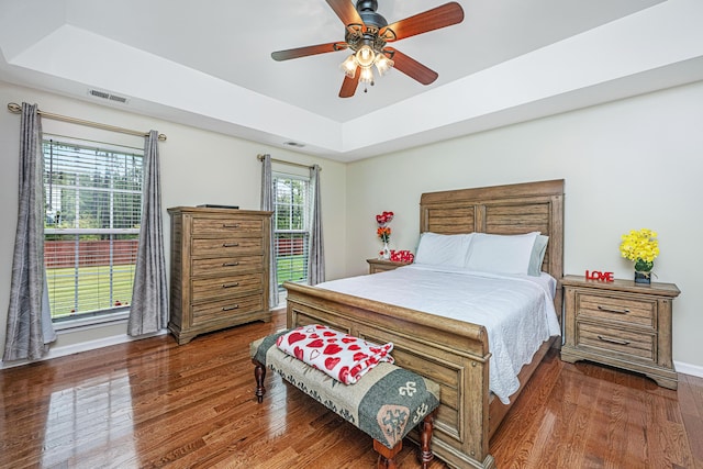 bedroom with a tray ceiling, ceiling fan, and dark wood-type flooring