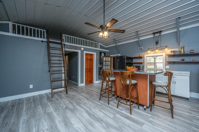 kitchen featuring ceiling fan, black fridge, a kitchen bar, white cabinets, and light wood-type flooring