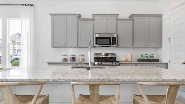 kitchen with a kitchen breakfast bar, gray cabinets, stainless steel appliances, and light stone counters