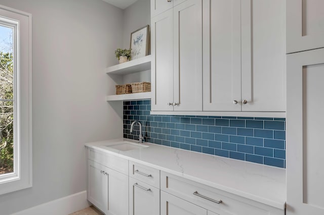 kitchen with tasteful backsplash, white cabinets, light stone countertops, open shelves, and a sink