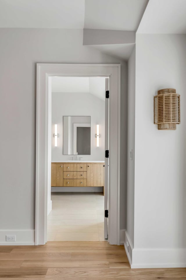 corridor with lofted ceiling, a sink, and light wood-style flooring