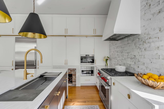 kitchen featuring sink, high end appliances, white cabinetry, hanging light fixtures, and custom range hood