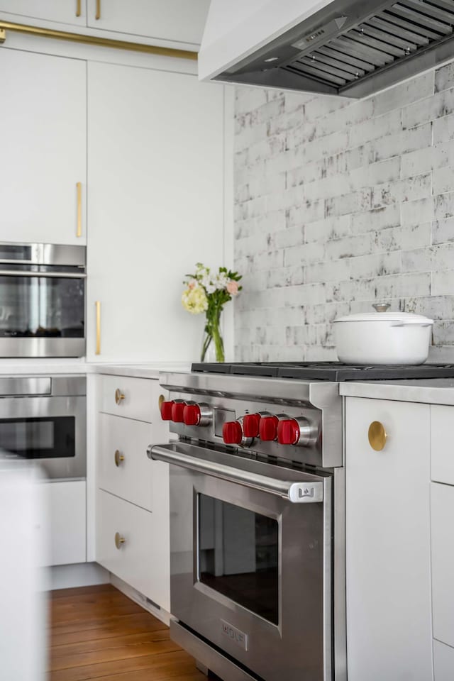 kitchen with designer stove, white cabinets, light wood-type flooring, and wall chimney exhaust hood