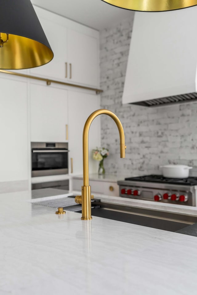 room details featuring white cabinets, oven, backsplash, and wall chimney exhaust hood