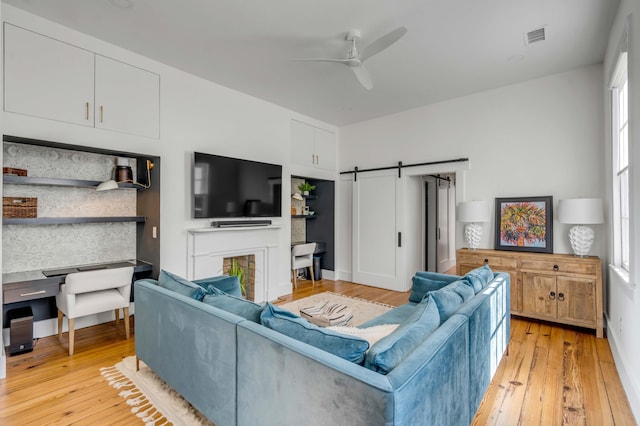 living room with ceiling fan, a barn door, and light hardwood / wood-style flooring