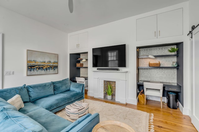 living room with a barn door, ceiling fan, and light wood-type flooring