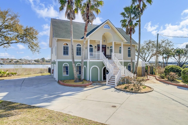 beach home with stairway, covered porch, concrete driveway, and a water view