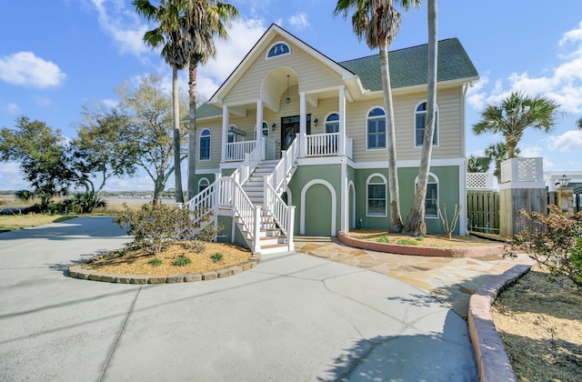 coastal inspired home with stairway, a porch, driveway, and fence