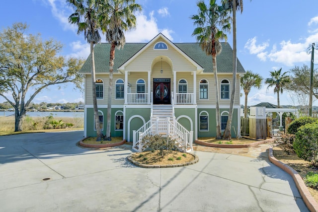 coastal inspired home with a porch, stairway, a water view, and driveway