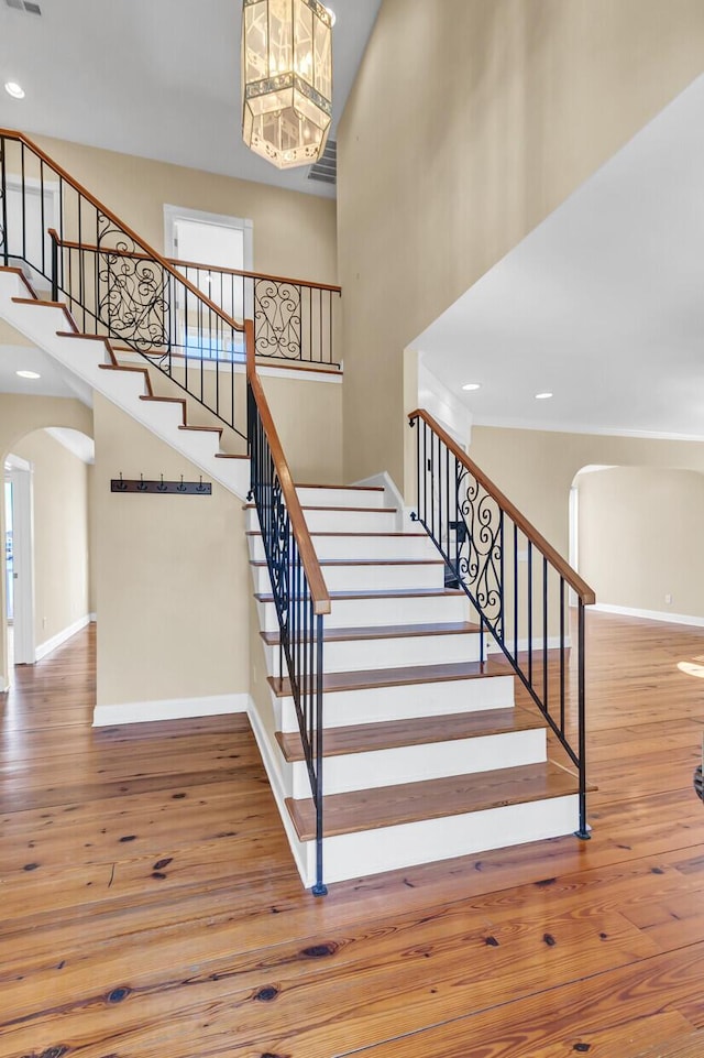 staircase with hardwood / wood-style floors, a high ceiling, baseboards, and arched walkways