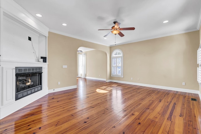 unfurnished living room with baseboards, a fireplace, arched walkways, wood-type flooring, and crown molding