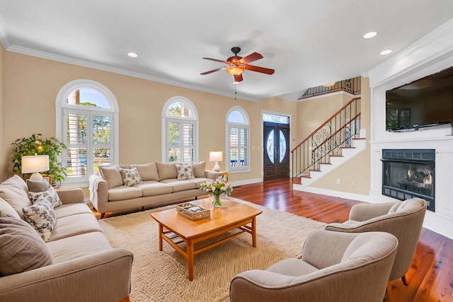 living room with a glass covered fireplace, stairway, wood finished floors, and ornamental molding