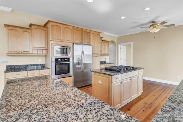 kitchen featuring light brown cabinets, a center island, dark stone counters, light wood-style floors, and stainless steel appliances