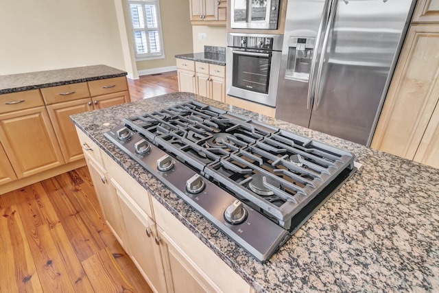 kitchen with dark stone counters, light wood finished floors, light brown cabinets, and appliances with stainless steel finishes