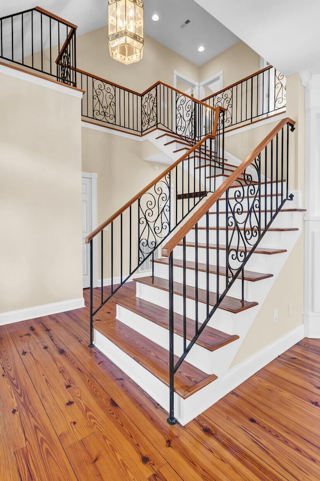 stairway featuring baseboards, wood finished floors, and a towering ceiling