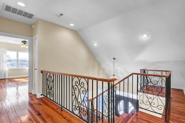 hall with an upstairs landing, visible vents, vaulted ceiling, and wood-type flooring