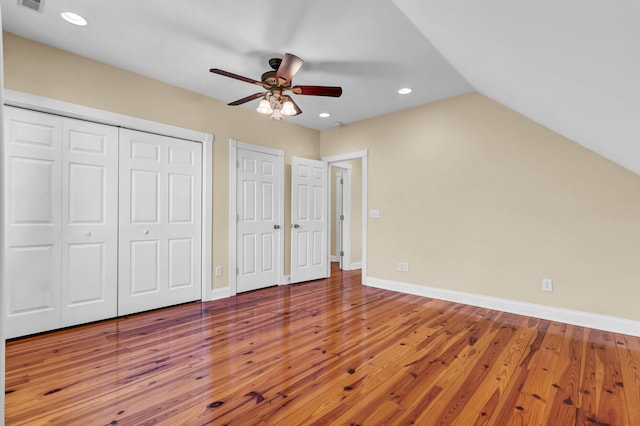 unfurnished bedroom with baseboards, vaulted ceiling, multiple closets, and hardwood / wood-style flooring