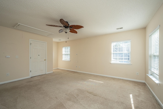 unfurnished room featuring ceiling fan, light colored carpet, a healthy amount of sunlight, and a textured ceiling