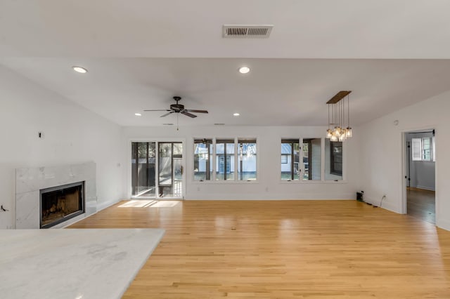 unfurnished living room featuring ceiling fan with notable chandelier, a high end fireplace, and light hardwood / wood-style flooring