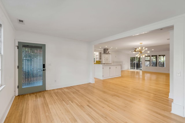 unfurnished living room with an inviting chandelier, crown molding, and light hardwood / wood-style flooring