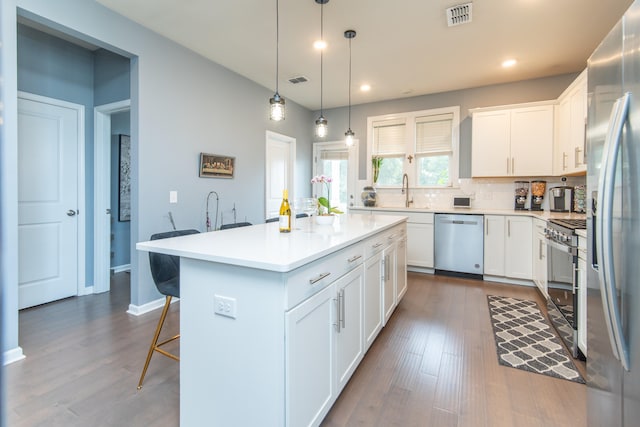 kitchen with appliances with stainless steel finishes, hardwood / wood-style flooring, a kitchen island, and white cabinetry