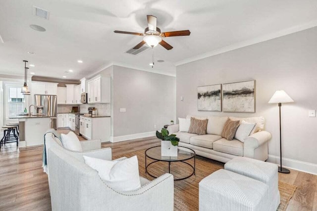 living room featuring ornamental molding, light hardwood / wood-style flooring, ceiling fan, and sink