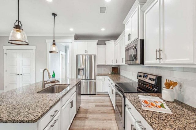 kitchen with stainless steel appliances, white cabinetry, sink, decorative light fixtures, and an island with sink