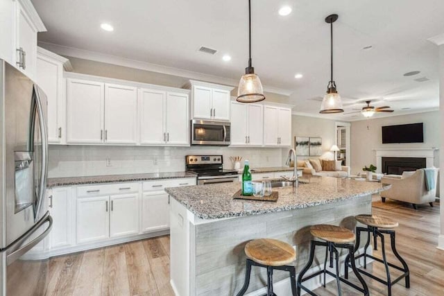 kitchen featuring stainless steel appliances, white cabinetry, pendant lighting, and light hardwood / wood-style flooring