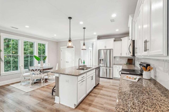 kitchen featuring appliances with stainless steel finishes, sink, white cabinets, dark stone countertops, and a kitchen island with sink