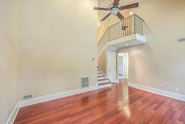 unfurnished living room with hardwood / wood-style flooring, ceiling fan, and a towering ceiling