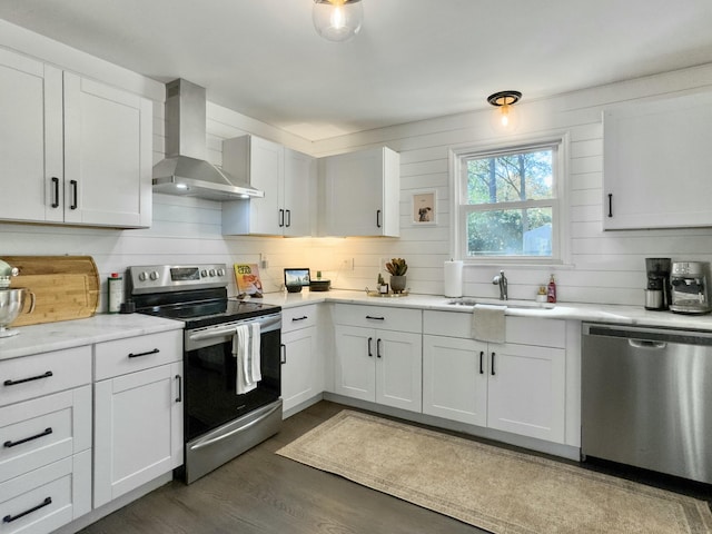 kitchen featuring wall chimney exhaust hood, stainless steel appliances, light countertops, white cabinetry, and a sink