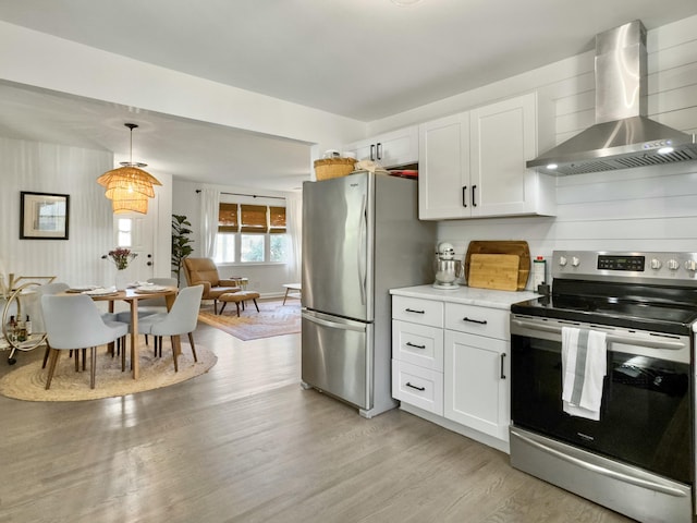 kitchen with appliances with stainless steel finishes, light countertops, white cabinetry, and wall chimney range hood