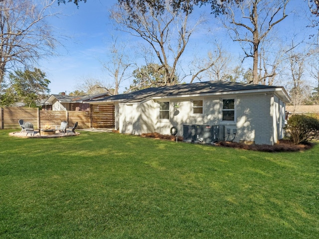 rear view of house featuring a fire pit, a yard, brick siding, and fence