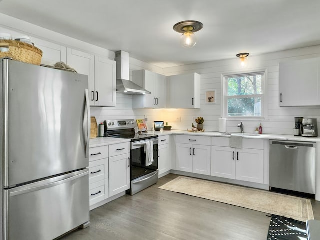 kitchen featuring stainless steel appliances, light countertops, white cabinetry, a sink, and wall chimney range hood