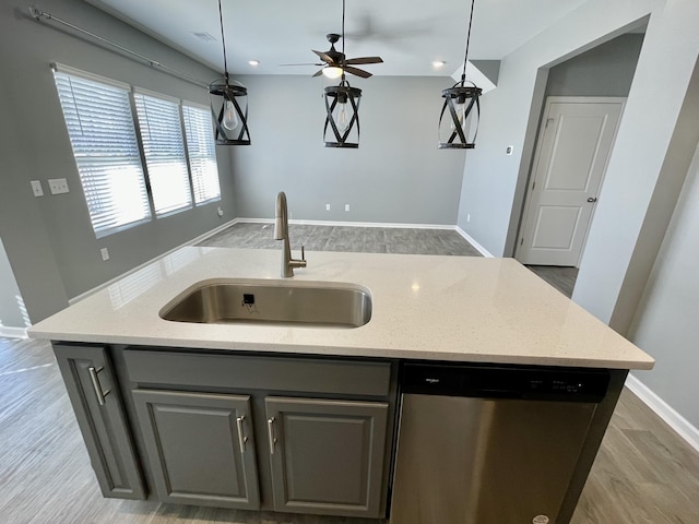 kitchen with light stone counters, sink, dishwasher, and a center island with sink