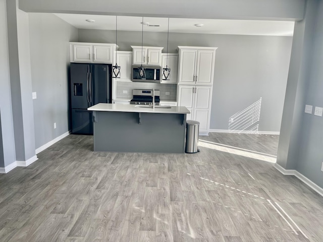 kitchen with appliances with stainless steel finishes, a kitchen island with sink, white cabinets, and decorative light fixtures