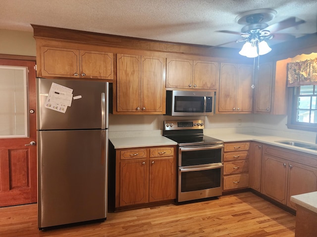 kitchen with stainless steel appliances, sink, a textured ceiling, light hardwood / wood-style floors, and ceiling fan