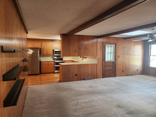 kitchen with appliances with stainless steel finishes, kitchen peninsula, light carpet, ceiling fan, and beam ceiling