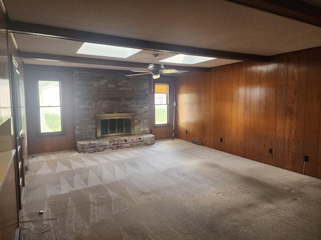 unfurnished living room with light carpet, a healthy amount of sunlight, beam ceiling, and a skylight