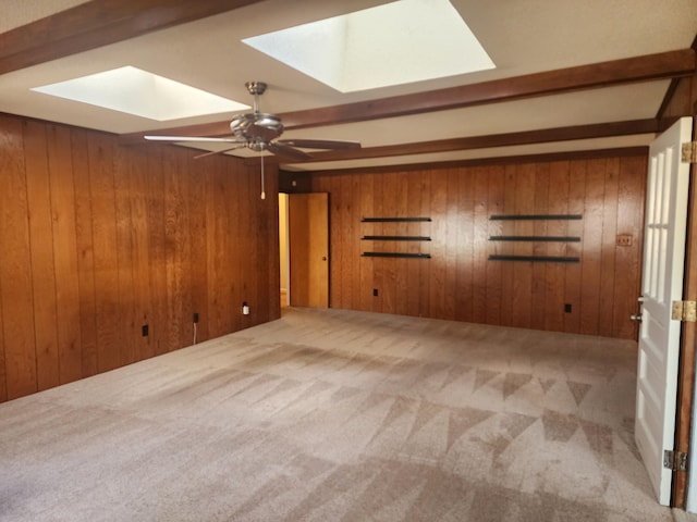 spare room with beamed ceiling, a skylight, ceiling fan, and wood walls