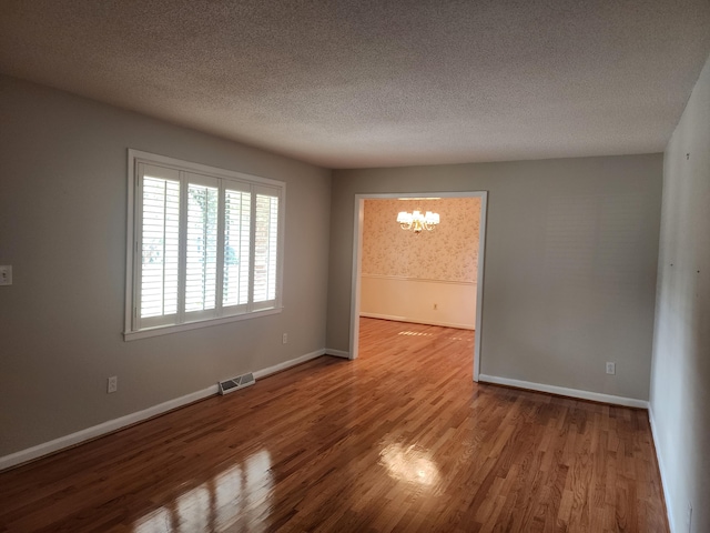 unfurnished room with a textured ceiling, hardwood / wood-style flooring, and an inviting chandelier