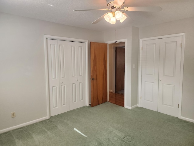 unfurnished bedroom with ceiling fan, multiple closets, a textured ceiling, and carpet floors