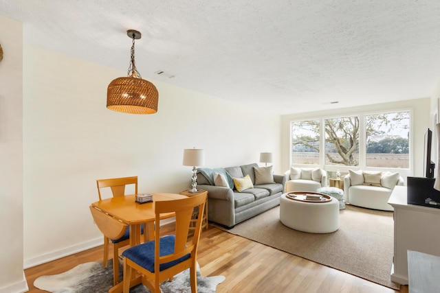 living area featuring baseboards, a textured ceiling, visible vents, and wood finished floors