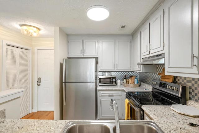 kitchen with tasteful backsplash, stainless steel appliances, a textured ceiling, under cabinet range hood, and a sink