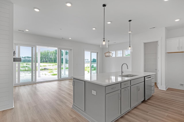 kitchen with gray cabinetry, dishwasher, sink, hanging light fixtures, and an island with sink