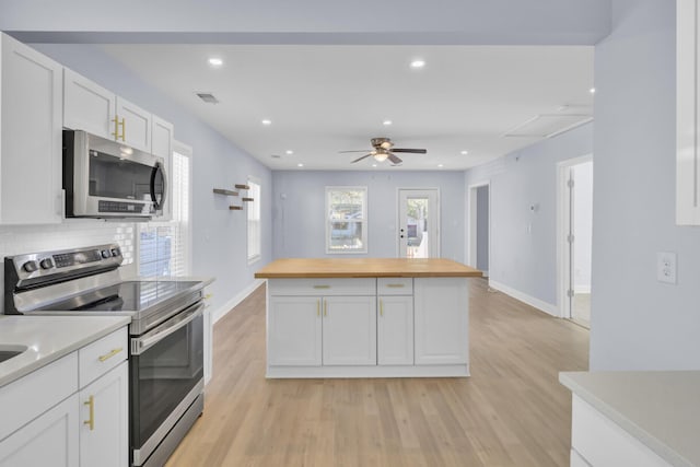 kitchen with appliances with stainless steel finishes, wood counters, white cabinetry, backsplash, and light hardwood / wood-style flooring